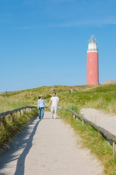 A peaceful scene unfolds as two individuals stroll along a path near a charming lighthouse in Texel, Netherlands. a couple of man and woman at The iconic red lighthouse of Texel Netherlands