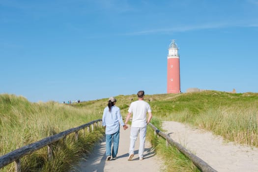 A couple leisurely walks along a scenic path beside the Texel lighthouse, enjoying the stunning view of the surrounding landscape. man and woman at The iconic red lighthouse of Texel Netherlands