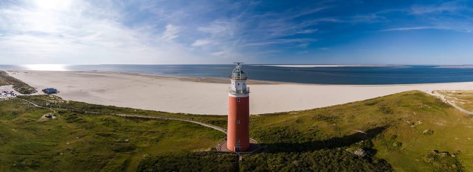 A birds eye view of a tall lighthouse with a beacon shining brightly on a sandy beach, overlooking the vast ocean on the island of Texel, Netherlands.