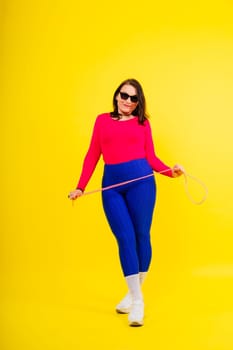 Pretty smiling plump female in a sporty top and leggings holding jumping rope in hands