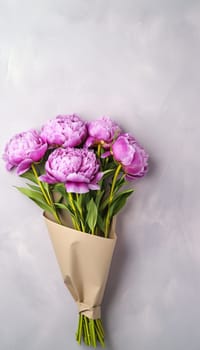 Man holding elegant pink peonies bouquet in craft paper against a clean white wall with copy space