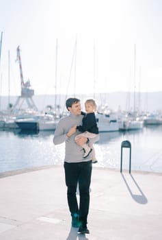 Smiling dad looking at little girl in his arms while walking on pier. High quality photo