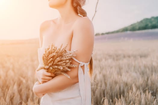 A woman is holding a bunch of wheat in her arms. The wheat is dry and brown, and the woman is wearing a white dress. The scene is set in a field, and the woman is posing for a photo