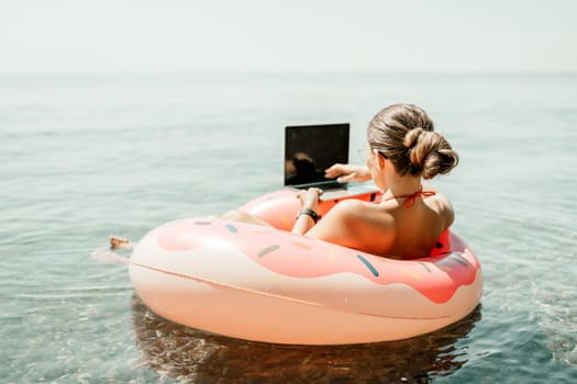 Woman laptop sea. Freelancer woman in sunglases floating on an inflatable big pink donut with a laptop in the sea. People summer vacation rest lifestyle concept