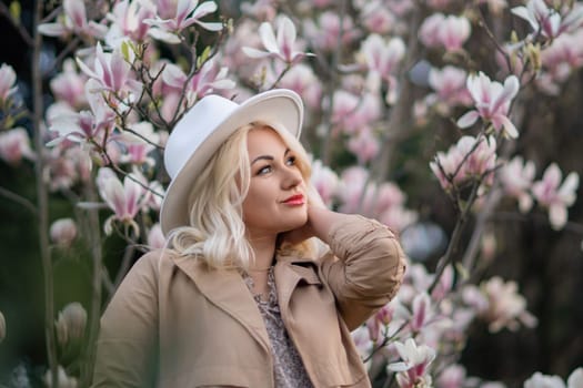 Magnolia flowers woman. A blonde woman wearing a white hat stands in front of a tree full of pink flowers. She is wearing a brown jacket and a necklace