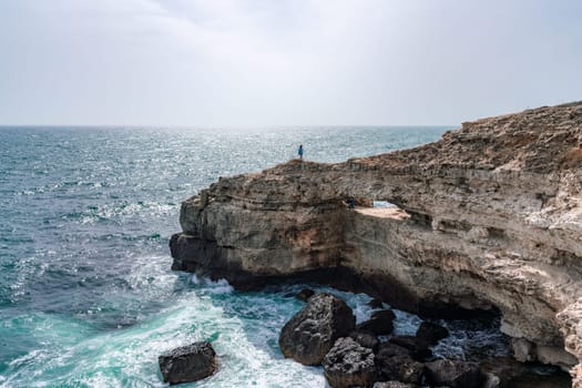 A rocky cliff overlooks the ocean, with the water crashing against the rocks. The scene is serene and peaceful, with the sound of the waves providing a calming atmosphere