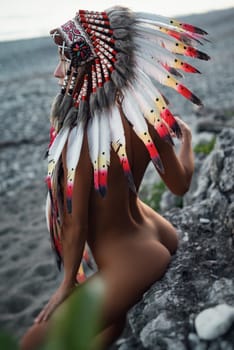 Naked sexy girl in Native American headdresses on the background of nature in beautiful sunset light