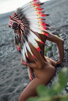 Naked sexy girl in Native American headdresses on the background of nature in beautiful sunset light