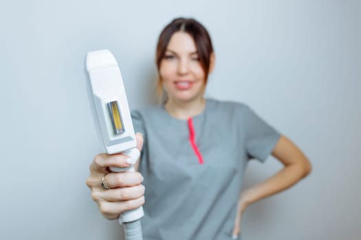 Female cosmetologist in a medical coat holds a working part of the modern laser epilator in her hands and poses for a photo. Laser epilation treatment in cosmetic beauty clinic