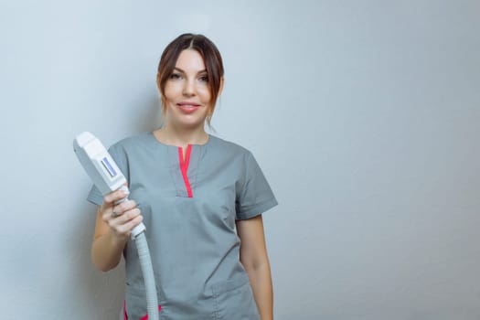 Female cosmetologist in a medical coat holds a working part of the modern laser epilator in her hands and poses for a photo. Laser epilation treatment in cosmetic beauty clinic