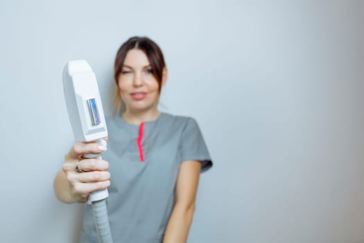 Female cosmetologist in a medical coat holds a working part of the modern laser epilator in her hands and poses for a photo. Laser epilation treatment in cosmetic beauty clinic
