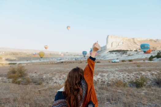 Excited woman with arms raised in front of colorful hot air balloons floating in cappadocia, turkey