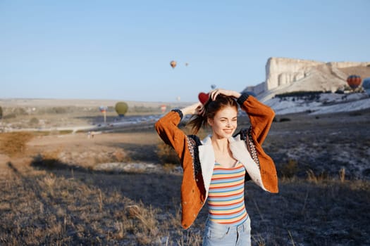 Woman in striped shirt standing in front of mountain with hot air balloons in background