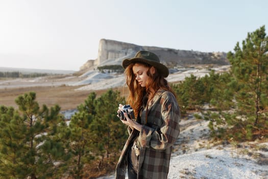 Stylish woman in plaid shirt and hat capturing a moment with vintage camera in outdoor setting