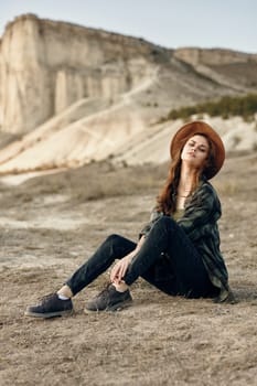 Serene young woman in hat sitting in desert with mountains in background on sunny day