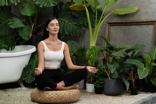 Young woman doing morning yoga and meditation in natural garden with plant leaf, enjoying the solitude and practicing meditative poses. Mindfulness activity and healthy mind lifestyle. Blithe