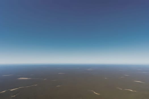 Looking out the window of an airplane, the camera captures a vast expanse of blue sky with fluffy white clouds passing by. The horizon can be seen in the distance, while the wing of the plane is partially visible in the frame.