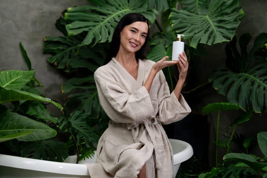 Tropical and exotic spa garden with bathtub in modern hotel or resort with woman in bathrobe holding beauty skincare product while enjoying leisure lush with greenery foliage background. Blithe