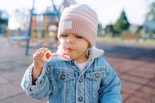 Little girl blowing soap bubbles on a sunny playground. High quality photo