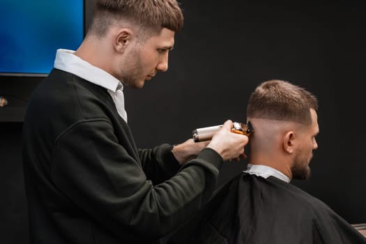 Young barber skillfully uses a trimmer to cut a mans hair