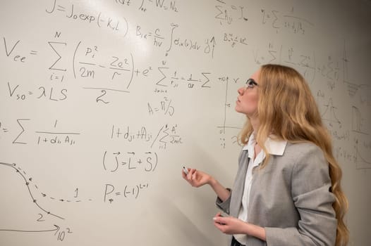 Young woman scientist writes formulas on a white board