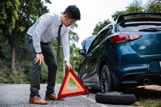 Man having car trouble and stranded at roadside with red warning triangle behind his broken car. Waiting for emergency assistance and transportation services.