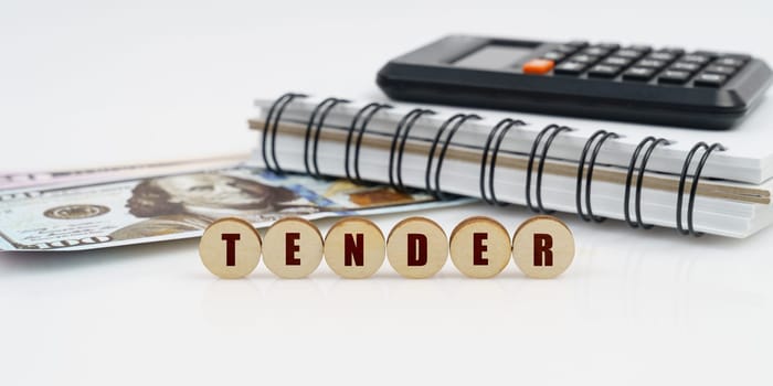 Business and finance concept. On a high surface lie a notepad, a calculator, dollars and wooden circles with the inscription - TENDER