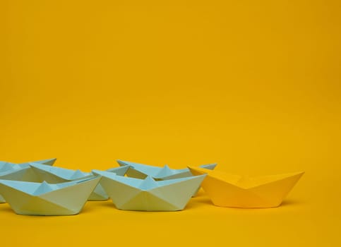 Group of blue paper boats follow yellow against a yellow background. Strong leader concept, mass manipulation. Starting a business with a well-coordinated team, start-up