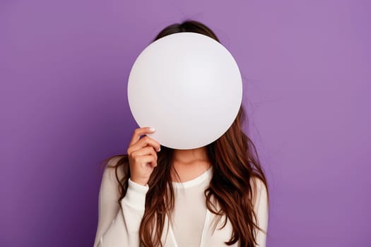 A woman holds a white balloon in front of her face.