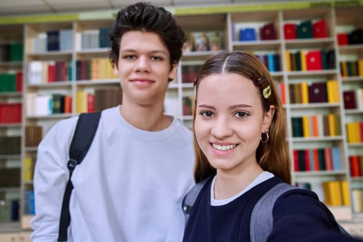 Selfie portrait of friends teenagers high school students looking at camera inside classroom. Having fun laughing teenage guy and girl in library. Friendship adolescence education lifestyle