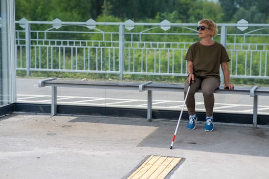 An elderly blind woman is waiting for transport at a bus stop