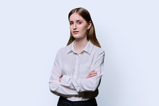 Portrait of young teenage smiling female in white shirt with crossed arms on white studio background. Confident beautiful happy college student girl looking at camera