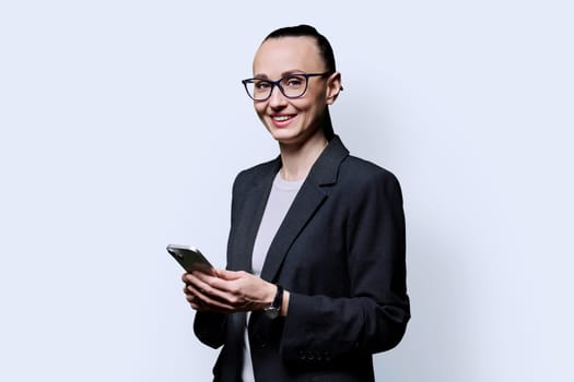 Adult smiling woman holding smartphone on white background. 30s female looking at camera with phone in hands. Technologies mobile applications internet work business leisure communication