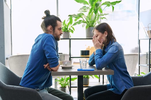 Serious aggressive young couple quarreling, angry, arguing, talking, nervous, sitting together at table in cafeteria. Relationships difficulties problems negative emotions lifestyle people concept