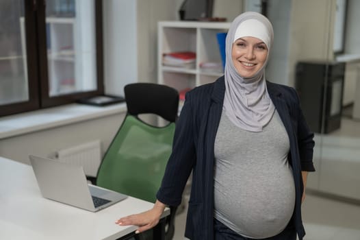 Pregnant Caucasian woman in hijab working in the office