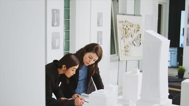 Two architects measuring building scale on blueprint, working together to create sketch of home layout. Team of developers drawing lines and elements on engineering drafts in agency office.