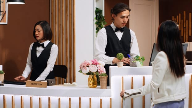 Receptionist examining passport information to do check in for customer, asian woman arriving at front desk after long flight. Employee doing id verification to confirm reservation. Handheld shot.