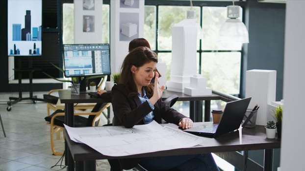 Sketch engineer meeting with contractor on videocall connection, discussing about scale measurements and draft elements before starting construction. Woman using online teleconference network.