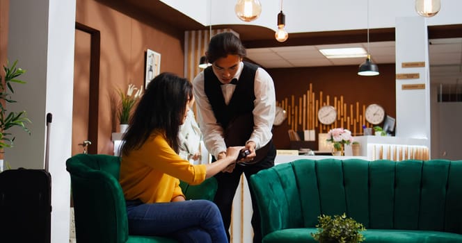 Woman traveler paying for coffee on pos terminal, buying drink to relax after long flight. Client sitting in lounge area waiting for check in, making electronic transaction with credit card.