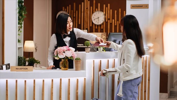 Front desk staff giving passport and access room card to client, finishing check in process and offering concierge services to asian guest. Woman receiving key and starting vacation at hotel.