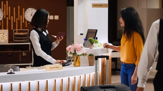 Asian hotel staff checking passport for id at check in, does verification for registration forms. Woman guest giving away documents to receptionist, arriving at five star holiday resort.