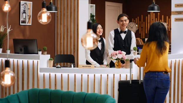 Front desk team greeting guest at five star hotel reception, welcoming person and ensuring easy check in procedure. Woman client entering lobby with luggage, hospitality industry.