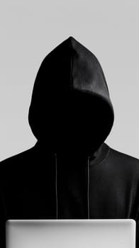 An anonymous hacker clad in a dark hoodie sits in front of an open laptop, their face obscured, set against grey backdrop - Generative AI