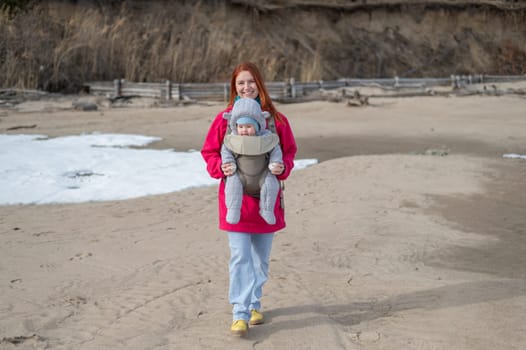 Caucasian red-haired woman walks with her son in an ergo backpack in nature in winter