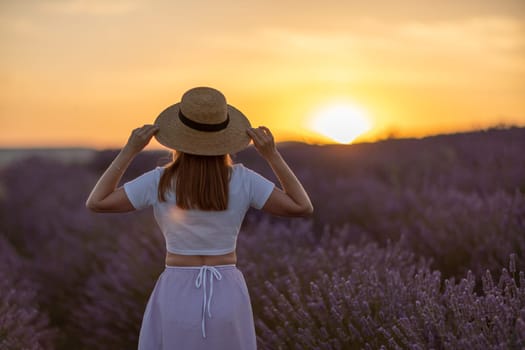 A woman wearing a straw hat stands in a field of lavender. The sun is setting in the background, casting a warm glow over the scene. The woman is enjoying the peacefulness of the moment
