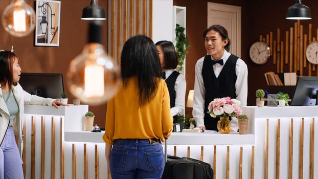 Hotel guests using service bell for assistance at front desk, calling for employees team to help with check in procedure upon their arrival. Two friends on holiday requesting support from staff.