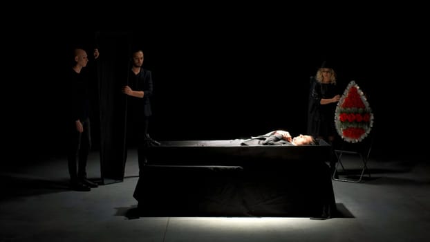 Theatrical funeral. Stock footage. Man in suit is buried on theater stage. Emotional stage production of funeral.