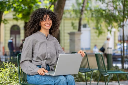 Caucasian young woman freelancer working online distant job with laptop browsing website chatting sitting outdoors. Lady girl on city street looking at notebook screen send messages watching movies