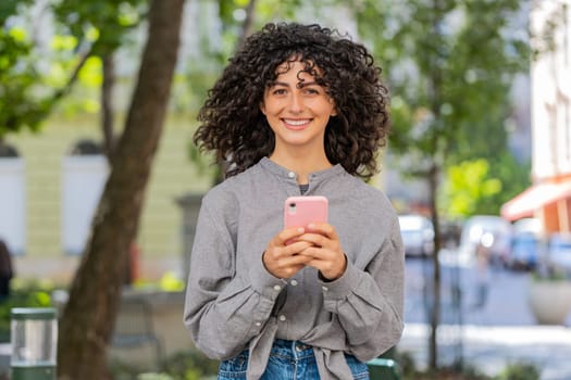 Close-up of Caucasian young woman using smartphone typing text messages in social media application online, surfing internet, relaxing, taking a break outdoors. Lady girl on city street. Sunny park