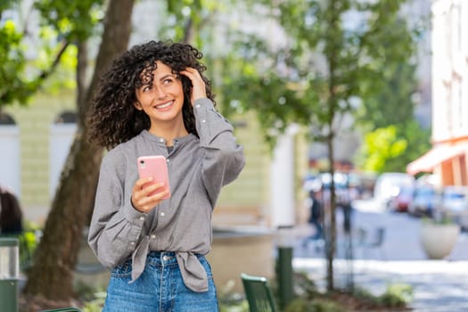 Close-up of Caucasian young woman using smartphone typing text messages in social media application online, surfing internet, relaxing, taking a break outdoors. Lady girl on city street. Sunny park
